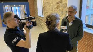 A cameraman, a woman with microphone interviewing a man